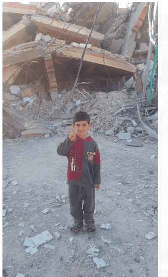 Childing posing with peace sign in front of destroyed apartment