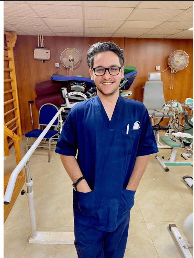 Man wearing scrubs in physician's room smiling